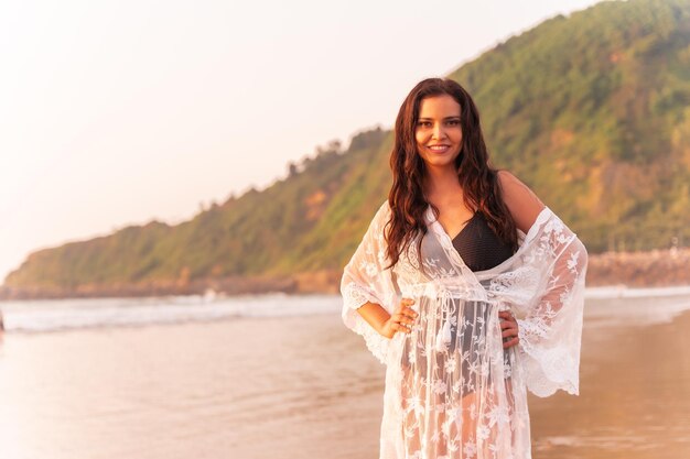 Ritratto di una donna al tramonto in un abito bianco che si gode l'estate in spiaggia