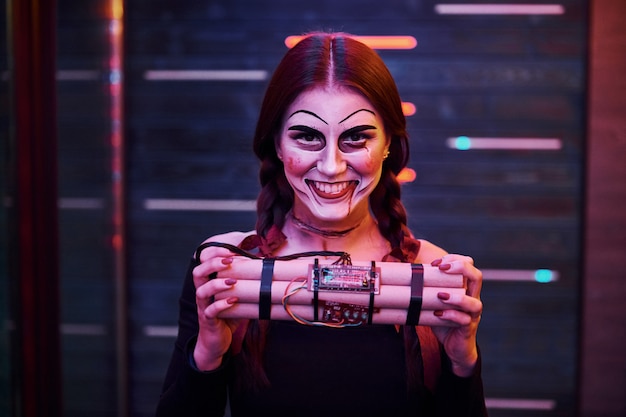 Portrait of woman that is on the thematic halloween party in scary makeup and costume with bomb in hands.