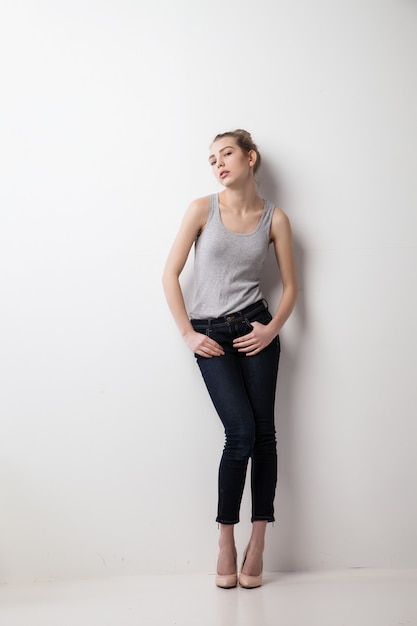 Portrait of woman in top and trousers standing against wall. Isolated over grey background.