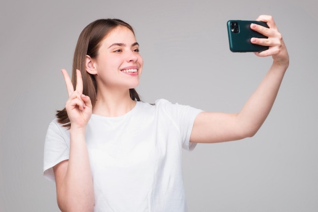휴대 전화를 사용하는 여성의 초상화 회색 배경 위에 스마트폰을 들고 있는 소녀 셀카를 찍는 소녀