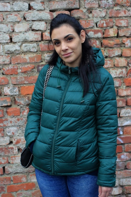 Portrait of woman in warm clothes standing against brick wall