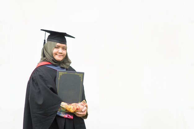 Foto ritratto di una donna che indossa un abito da laurea mentre tiene in mano un documento sullo sfondo bianco