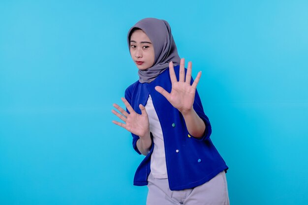 Portrait of a woman wearing hijab showing stop gesture on blue wall