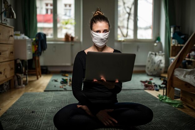 Photo portrait of woman wearing mask holding laptop at home