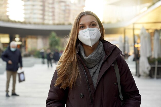 Portrait of woman wearing medical face mask in city street as prevention against virus looking at camera