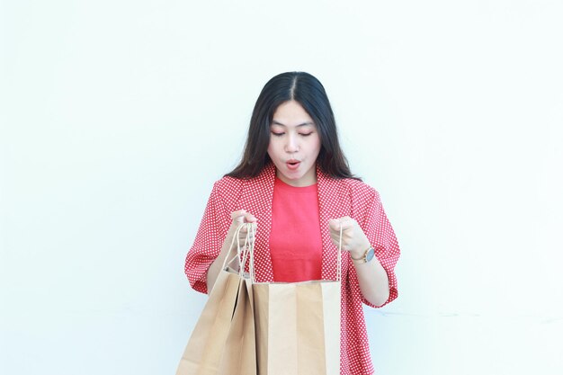 portrait woman wearing red outfit with surprised gesture looking at contents of shopping bag