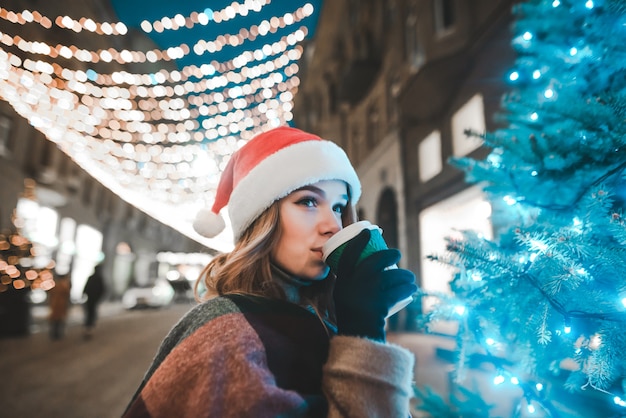 portrait woman wearing Santa hat holding cup of coffee