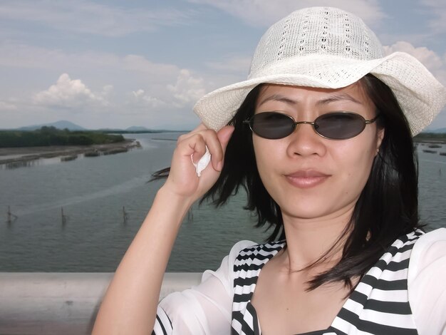 Foto ritratto di una donna che indossa occhiali da sole e un cappello contro il mare