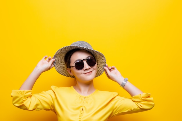 Portrait woman wearing sunglasses and hat isolated over yellow background