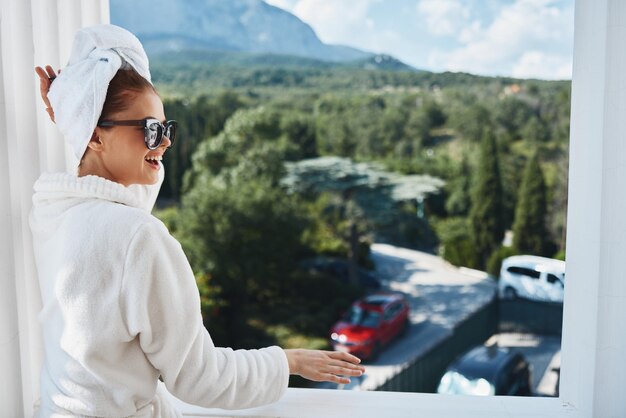 Portrait woman wearing sunglasses posing in a bathrobe on a\
balcony rest mountain view