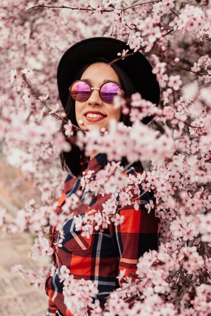 Foto ritratto di una donna con gli occhiali da sole in piedi vicino al fiore di ciliegio