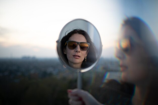 Foto ritratto di una donna che indossa occhiali da sole mentre si riflette sullo specchio