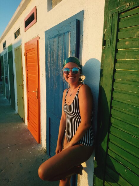 Foto ritratto di una donna che indossa occhiali da sole mentre si trova vicino alle case sulla spiaggia