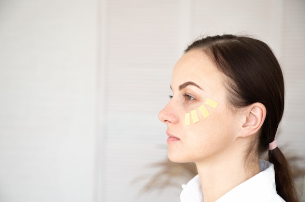 Portrait of a woman on a white background with a kinesiotape of the face. Aesthetic taping concept.