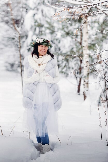 寒い冬の森で白い服を着た女性の肖像画。雪に覆われた冬の森で頭に花輪を捧げる少女