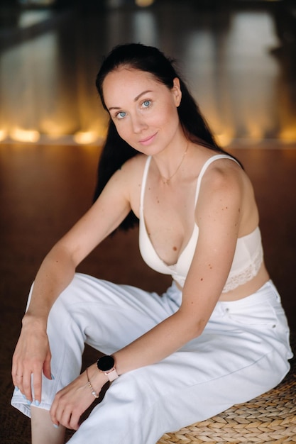 Photo portrait of a woman in white clothes sitting on an ottoman in the interior