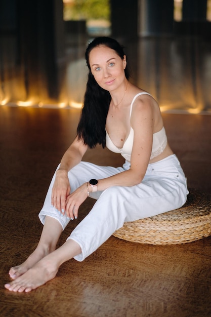 Portrait of a woman in white clothes sitting on an ottoman in the interior