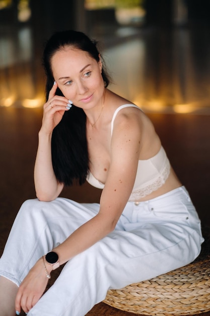 Portrait of a woman in white clothes sitting on an ottoman in the interior