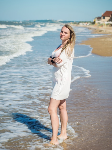 Portrait of a woman in a white dress with blinded by the sun face the sea.