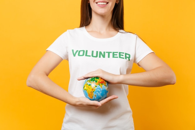 녹색 제목 자원 봉사자가 손바닥에 새겨진 흰색 티셔츠를 입은 여성의 초상화는 노란색 배경에 격리된 지구 세계입니다. 자발적인 무료 지원 도움, 자선 은혜 개념.