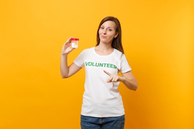 Портрет женщины в белой футболке, написанной надписью зеленым заголовком, волонтером, держащим бутылку с таблетками, изолированными на желтом фоне. Добровольная бесплатная помощь, концепция здоровья благодати благотворительности.