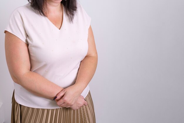 Portrait of a woman in a white tshirt and skirt with her hands folded on her stomach shot to the wai...