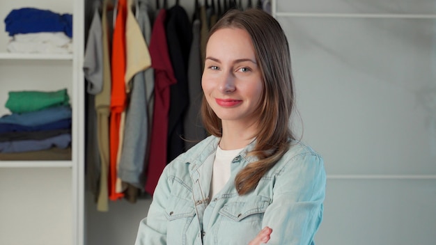 Portrait of a woman who stands against the background of a large wardrobe a wardrobe with stylish clothes and household items.