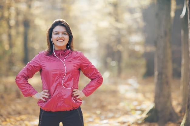 Portrait of a woman who trains and listens to music in the morning autumn park