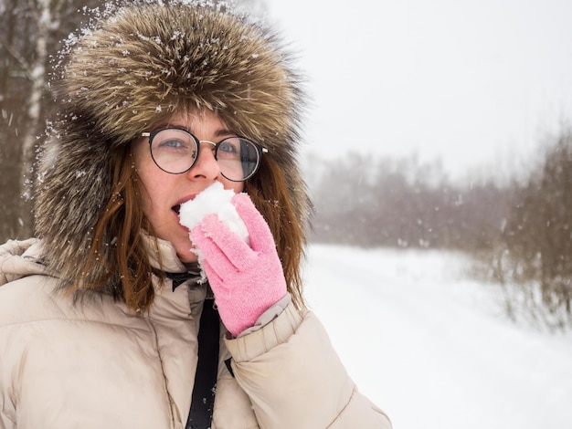 Portrait of a woman in winter clothes opening her mouth to eat white snow from her hand