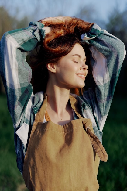 Portrait of a woman with a beautiful smile in her work clothes and apron in nature enjoying relaxation after work in the sunset sunlight