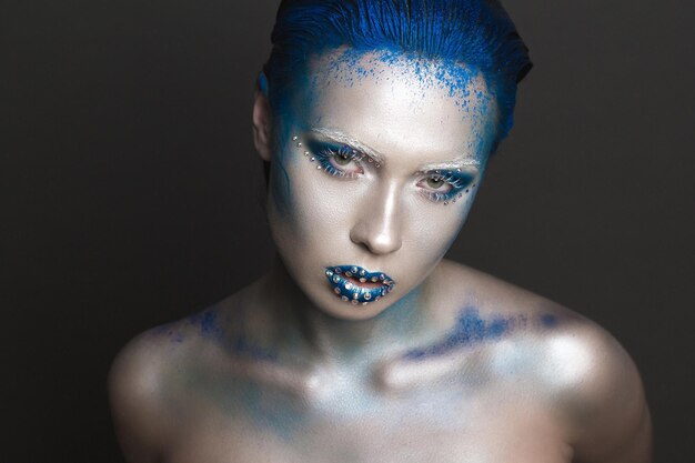 Photo portrait of woman with blue powder paint and make-up against black background