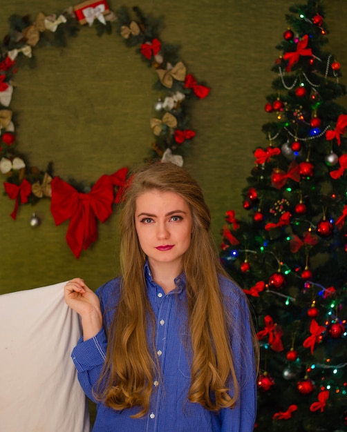 Portrait of a woman with bright red lips, blond long hair against the New Year tree. Young woman with a white pillow in his hands
