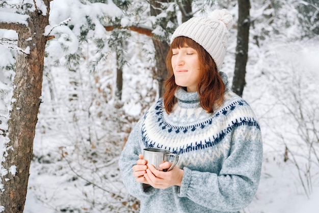 Portrait of a woman with a cup of tea in her hands on a background of snowy forest