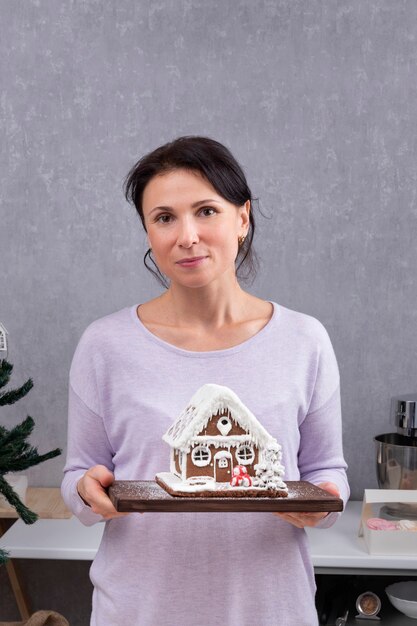 Portrait of woman with gingerbread house in her hands. New Years sweets. Vertical frame.