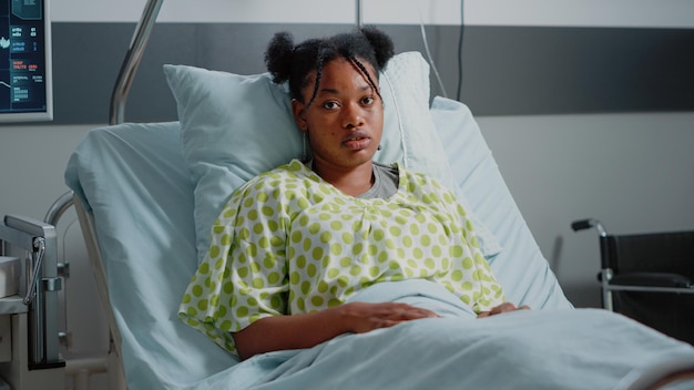 Portrait of woman with iv drip bag in hospital ward bed. young
patient with sickness preparing to receive healthcare treatment and
medicine against disease. ill person looking at camera