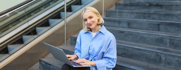 Portrait of woman with laptop found wifi spot sitting on stairs outdoors drinking coffee working on