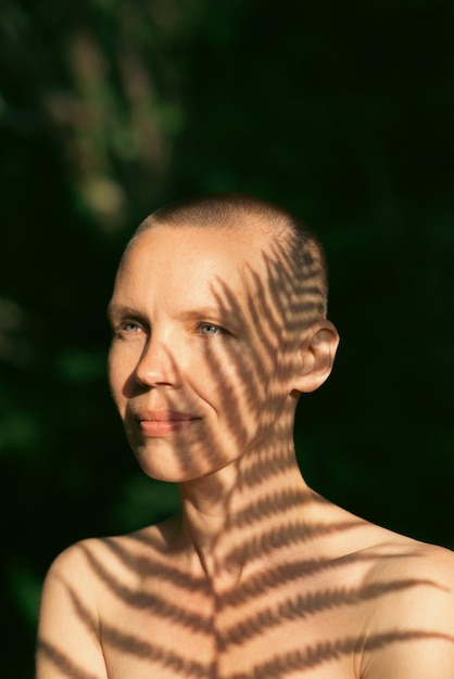 Foto ritratto di una donna con la testa rasata con le ombre di una felce nella ripresa naturale della foresta