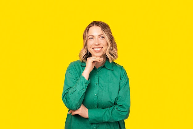 Portrait of a woman with short hair smiling at the camera waring a green shirt standing over yellow background