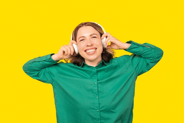 Photo portrait of a woman with short hair smiling at the camera while she is listening to the music waring a green shirt standing over yellow background