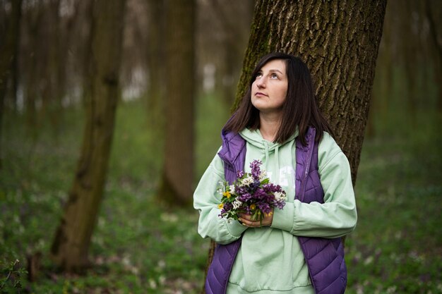 春の花を持つ女性の肖像画は森の木にもたれて自然への愛