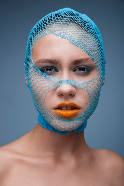 Portrait of woman with a torn blue stocking on her head on a blue background. Yellow lipstick