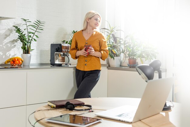 Portrait of woman working with laptop in bright kitchen. Covid-19 coronavirus. Social distancing