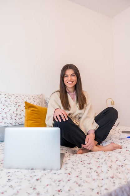 Portrait of a woman working with laptop sitting on the bed telecommuting teleworking