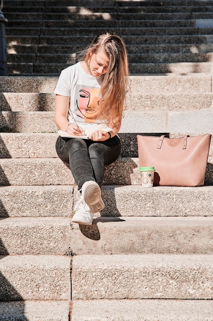 캐주얼 옷을 입고 야외 계단에 앉아 글을 쓰는 여성의 초상화