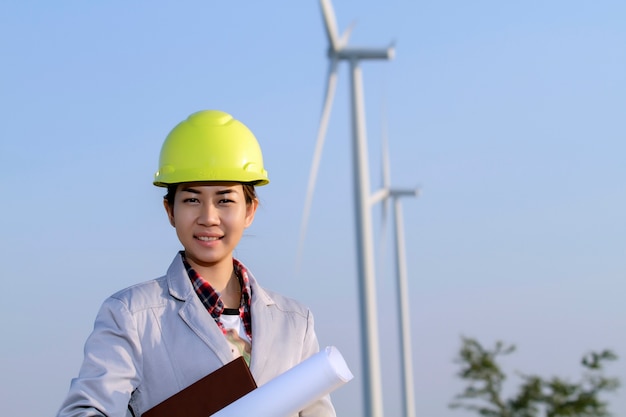 portrait women asia engineer working and holding blueprints at wind turbine farm