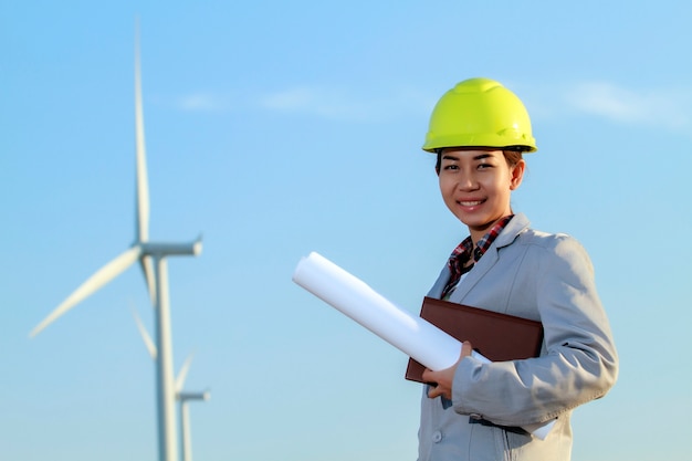 portrait women asia engineer working and holding blueprints at wind turbine farm