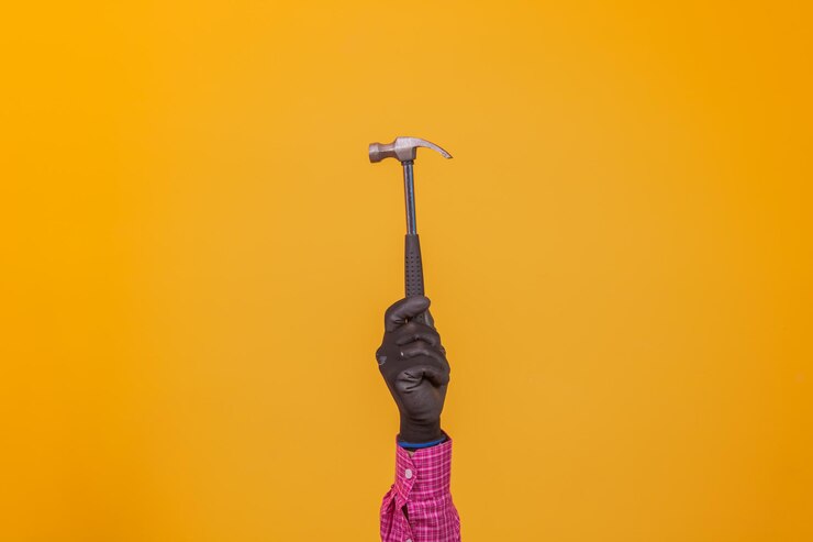 Portrait of a worker hand holding a hammer isolated on yellow background.
