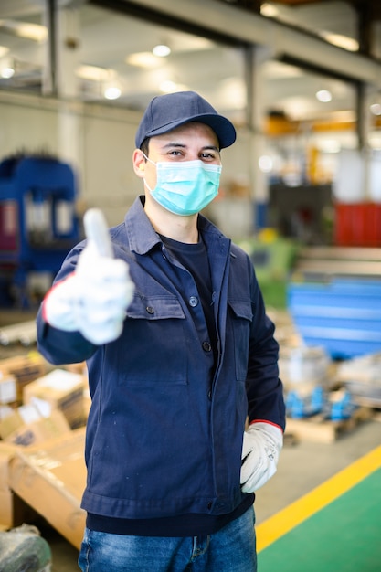 마스크를 착용하고 엄지 손가락, 코로나 바이러스 개념을 포기하는 산업 공장에서 노동자의 초상화