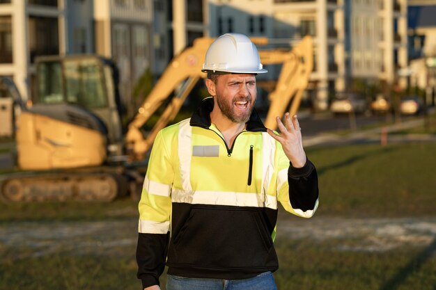 Portrait of worker man small business owner. Construction worker with hardhat helmet on construction site. Construction engineer worker in builder uniform with excavation truck digging. Worker constru