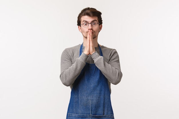 Portrait of worried hopeful young man nervously looking at customer reaction as giving coffee, learn how to make good drinks as work as barista, hold hands in pray concerned, 